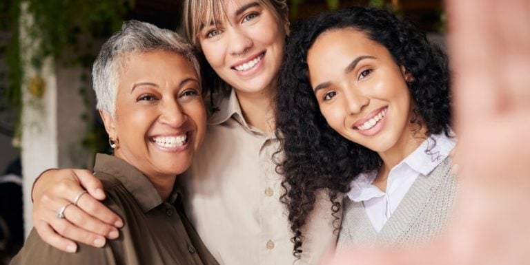 Elderly Woman Posing Happily with Two Younger Women Indoors at a Memory Care Facility