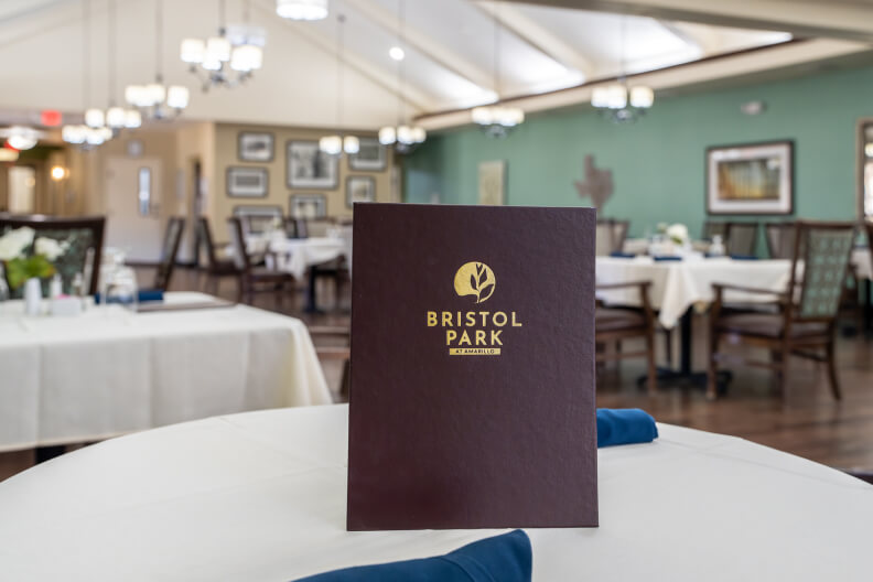 Restaurant Style Dining Room With Tables Chairs and Menu Display at Memory Care Facility Restaurant Style Dining Room With Tables Chairs and Menu Display at Memory Care Facility